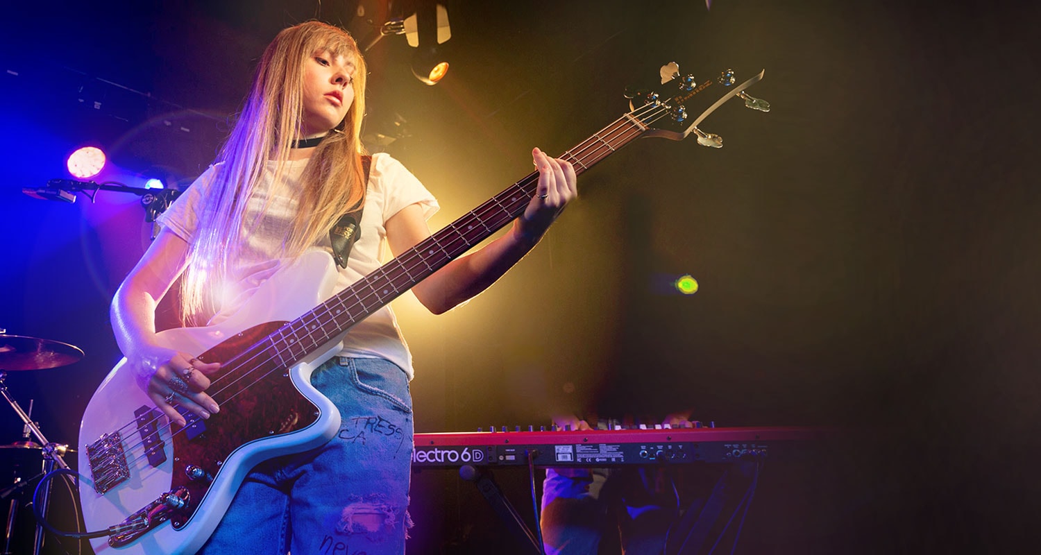 Young girl practicing 4 string bass on stage with her band.