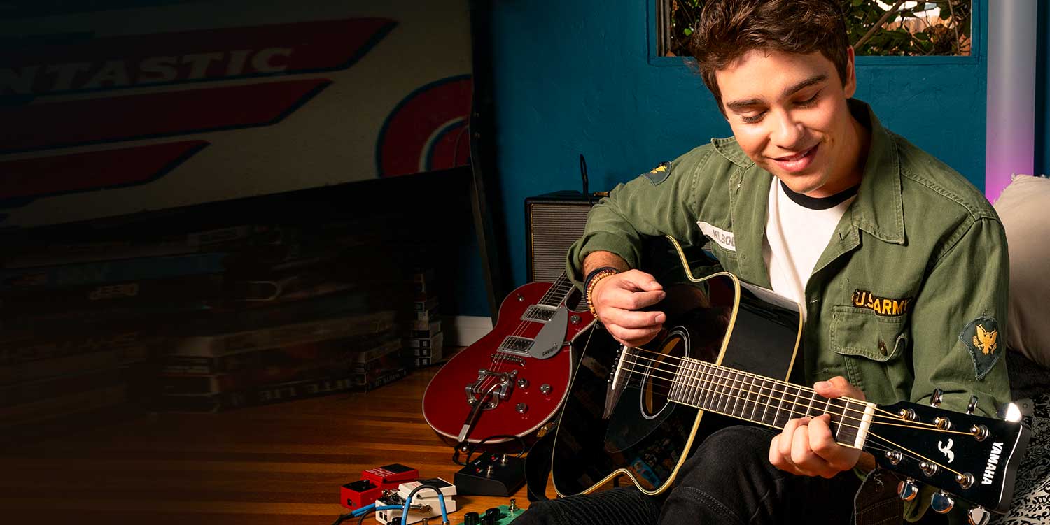 Teenager in green jacket strumming acoustic guitar.