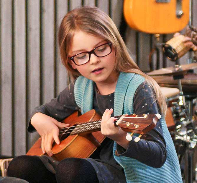 Child with glasses learning how to play the ukelele.