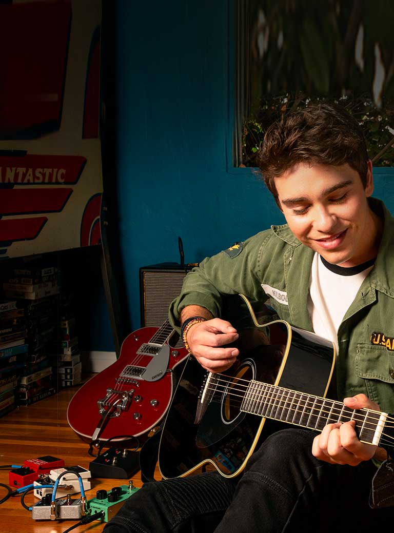 Teenager in green jacket strumming acoustic guitar.