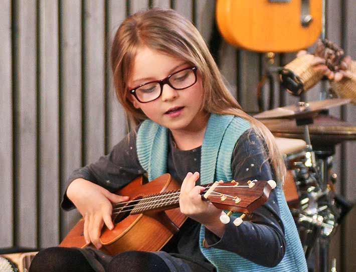 Child with glasses learning how to play the ukelele.