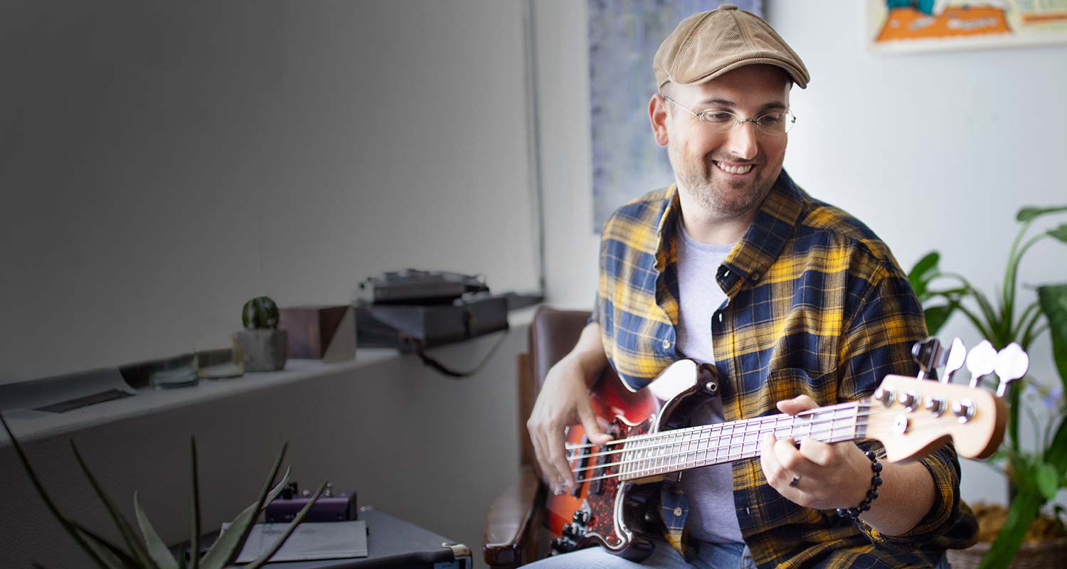 Man in hat and glasses playing bass guitar with instructor.