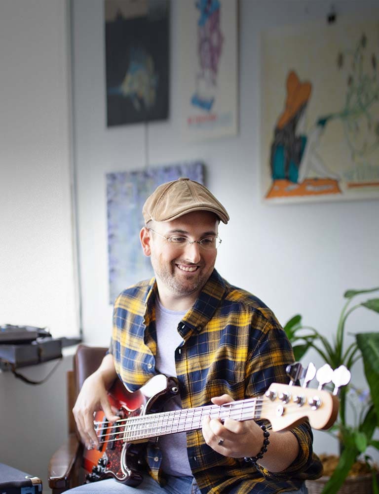 Man in hat and glasses playing bass guitar with instructor.