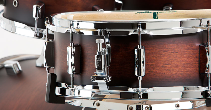 Pearl Decade Maple snare drum with matching finish, sticks resting on top, chrome throw-off visible, toms and cymbals in background