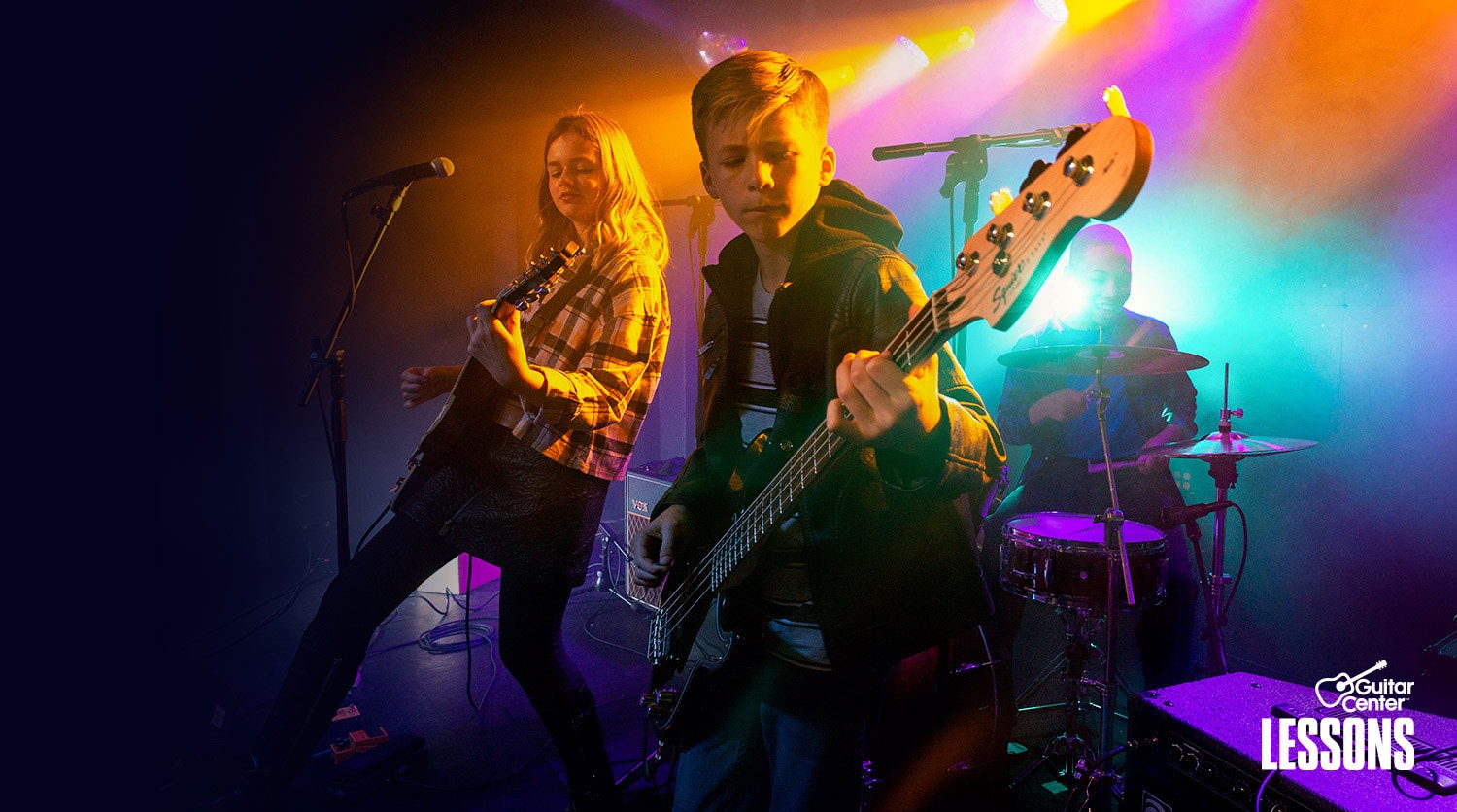 Teenager in t-shirt and blue jeans strumming 4 string bass guitar on stage.