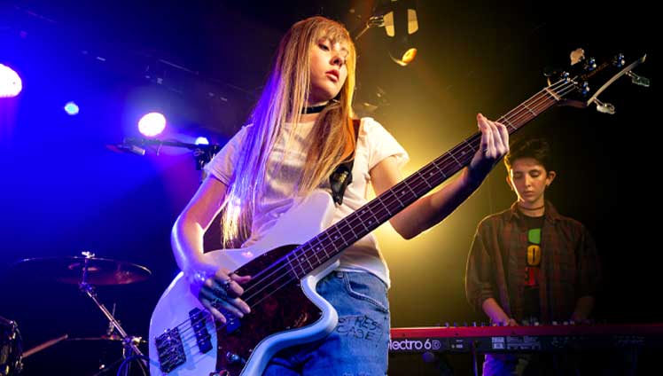 Young girl practicing 4 string bass on stage with her band.
