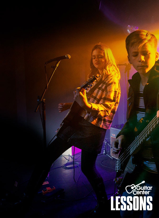 Teenager in t-shirt and blue jeans strumming 4 string bass guitar on stage.