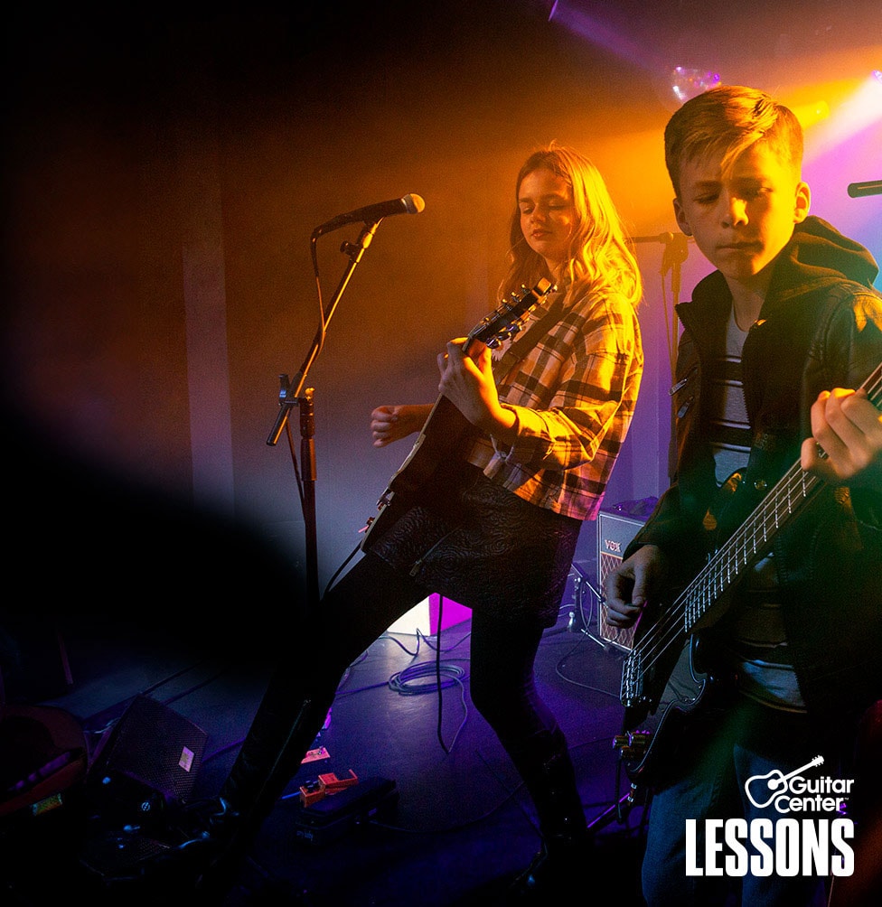 Teenager in t-shirt and blue jeans strumming 4 string bass guitar on stage.