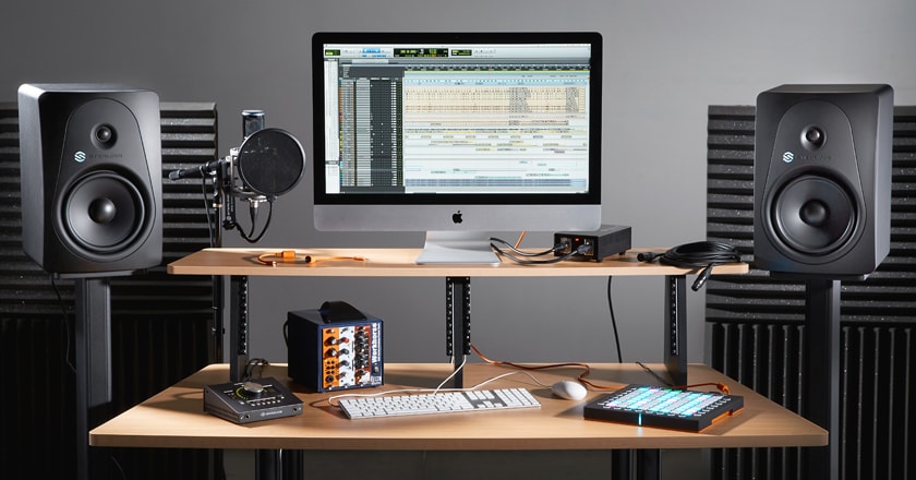 A project studio desk with recording equipment on it and two Sterling MX8 Studio Monitors setup as a stereo pair on stands.